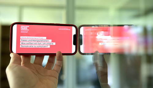 Smartphone anliegend an spiegelnder Glasscheibe mit Forum gegen Fakes Inhalt